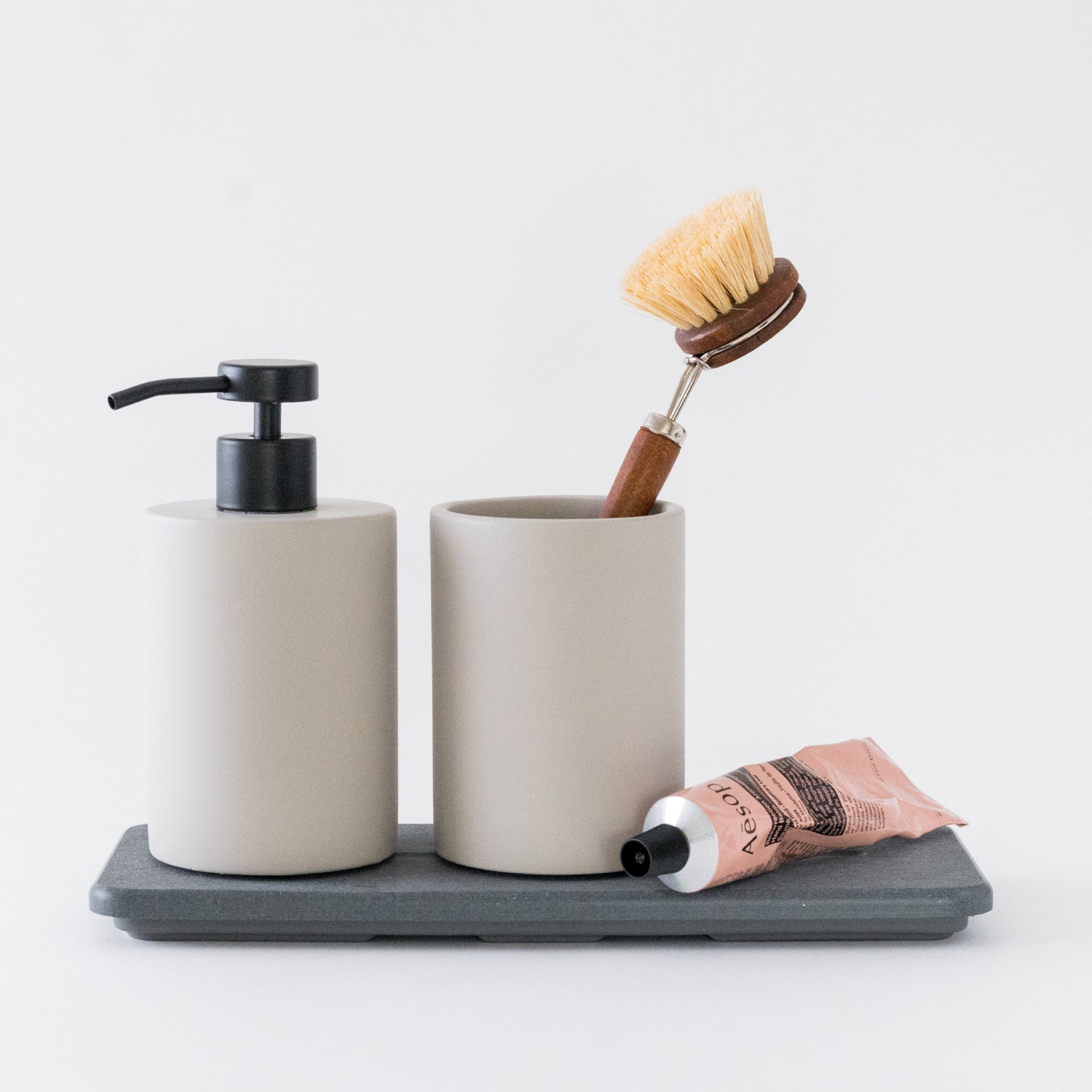 Bathroom set with soap dispenser, toothbrush holder, and tube of toothpaste on a gray tray.