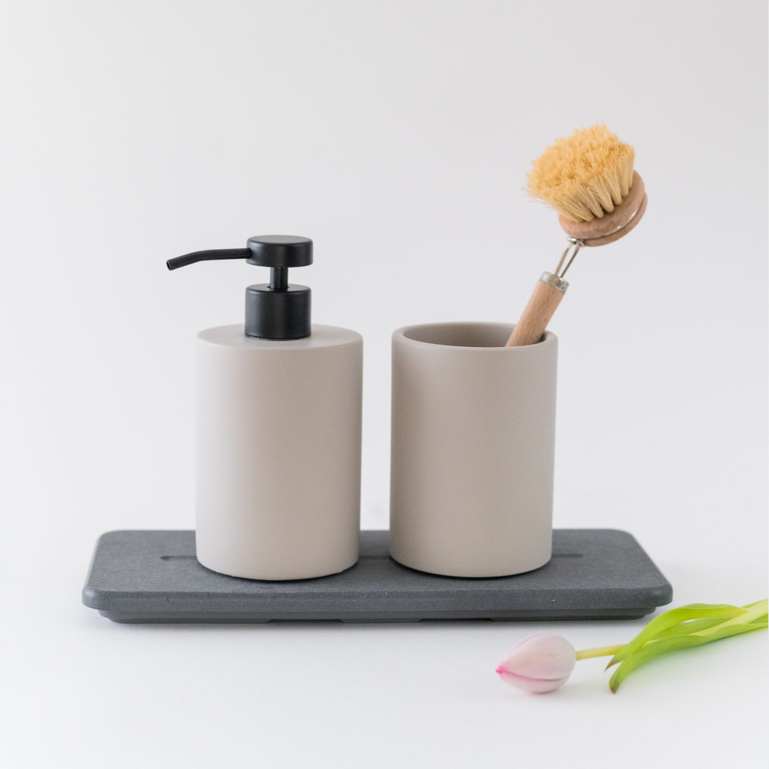 Bathroom set with beige dispenser, cup, and scrubber on a gray tray with tulips.