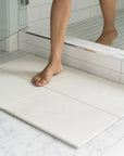 Woman stepping out of shower onto large bath stone mat sandstone 
